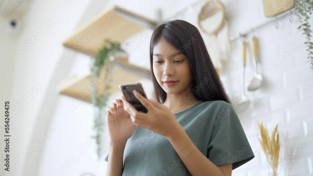 Happy young asian woman relaxing at home. Asia female standing at counter kitchen and using mobile smartphone Happy young asian woman relaxing at home. Asia female standing at counter kitchen and using mobile smartphone