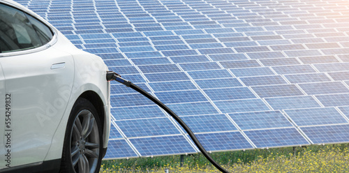 Close up of electric car with a connected charging cable on the background of solar panels 
