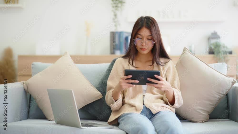 Young asian woman using computer laptop, tablet and mobile smartphone while seated on couch at home Young asian woman using computer laptop, tablet and mobile smartphone while seated on couch at home