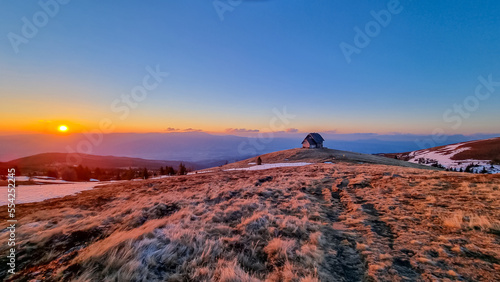 Scenic view of mountain hut Wolfsbergerhuette (Wolfsberger Huette) during sunrise on Saualpe, Lavanttal Alps, Carinthia, Austria, Europe. Snow covered meadow leading to remote alpine cottage photo