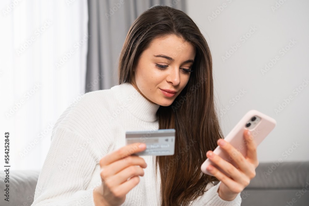 Young woman holding a credit card and using a mobile phone for paying. Online shopping and spending money for gifts concept. Young woman holding a credit card and using a mobile phone for paying. Online shopping and spending money for gifts concept.