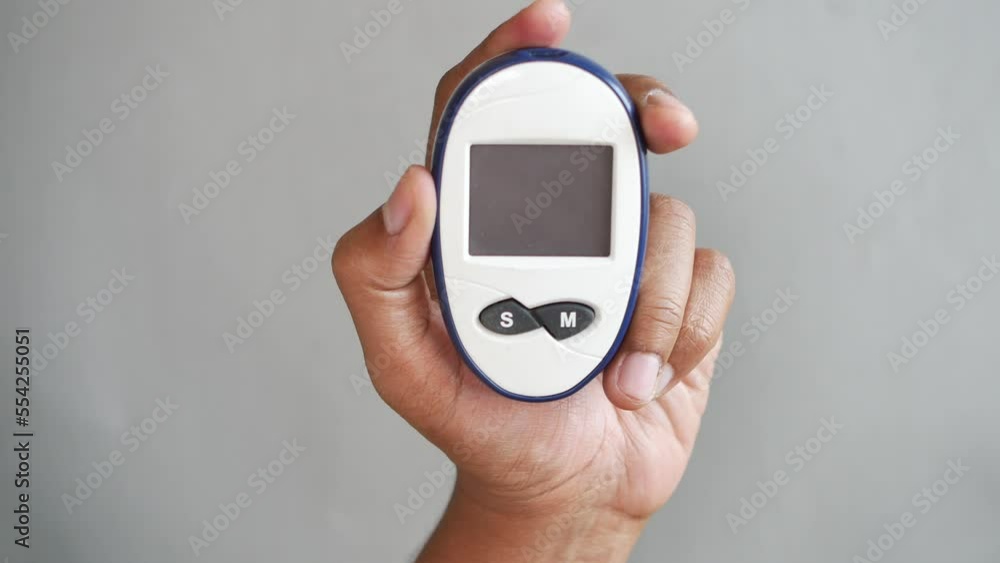 man's hand holding a glucose meter against gray background man's hand holding a glucose meter against gray background