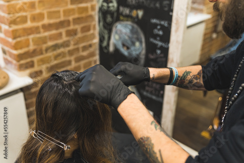 Professional hairdresser in the black hat with beard wearing black gloves dyeing his client's long hair in the professional hair salon. High quality photo