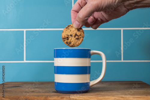 Foto Blue and white cup of tea with a hand dunking a chocolate chip biscuit cookie