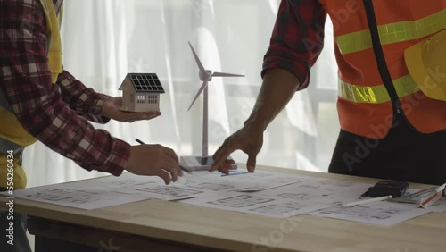 Asian engineer A foreman or leader discusses a home solar farm and a model of a wind turbine in a construction project office.