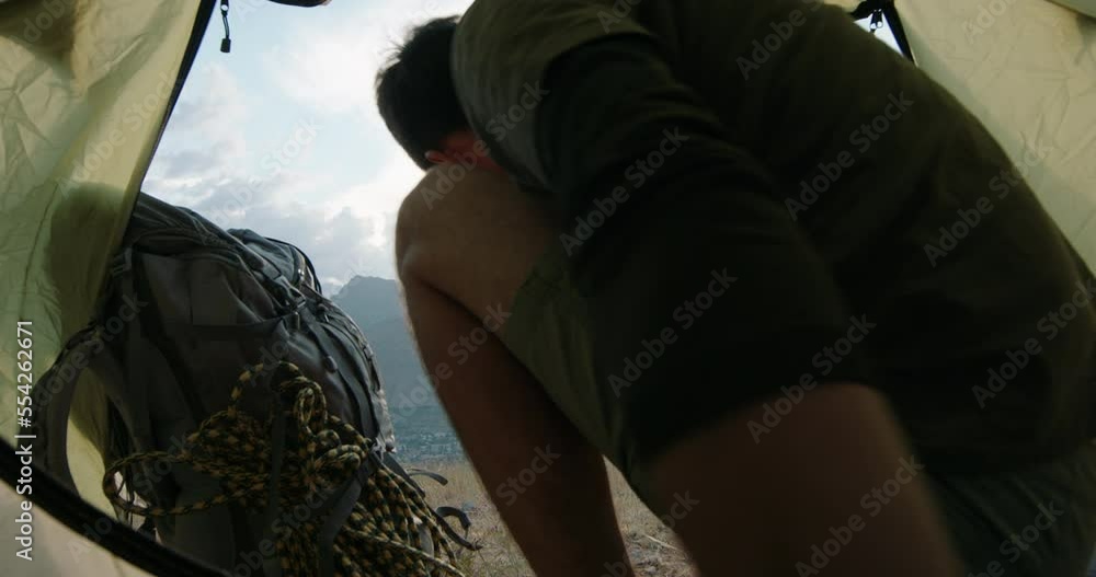 a young Caucasian male tourist-traveler in the mountains comes out of the tent in the early morning and raises his arms in the air. happy and drunk on life, youth and happiness a young Caucasian male tourist-traveler in the mountains comes out of the tent in the early morning and raises his arms in the air. happy and drunk on life, youth and happiness
