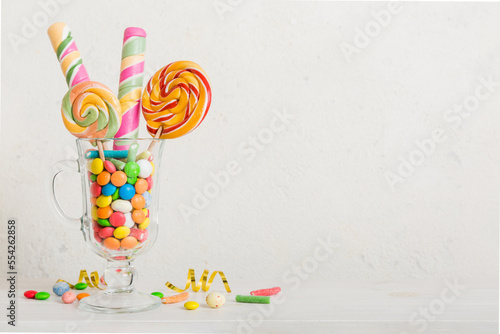 Colorful candies in cup on table on light background background. Large swirled lollipops. Creative concept of a jar full of delicious sweets from the candy store