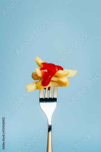 close-up of french fries with ketchup sauce chopped on a fork on a blue background