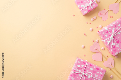Valentine's Day concept. Top view photo of pink present boxes paper hearts on sticks and sprinkles on isolated pastel beige background with empty space © ActionGP