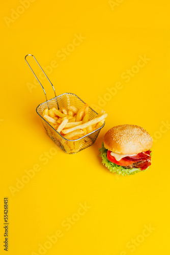 close-up of french fries in a basket and a hamburger on yellow background with free space for text