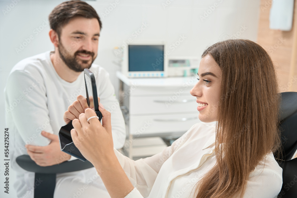 Obraz premium Pleased dental clinic client examining her teeth after treatment