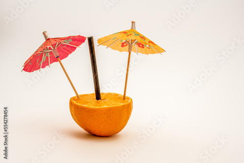 pair of colorful orange  and red party drinks parasol umberellas and black bamboo straw in half an orange photo