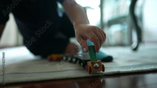 Child plays with traditional car wooden train toy on floor