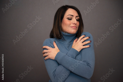 bella ragazza con maglione azzurro su sfondo nero che si accarezza  photo