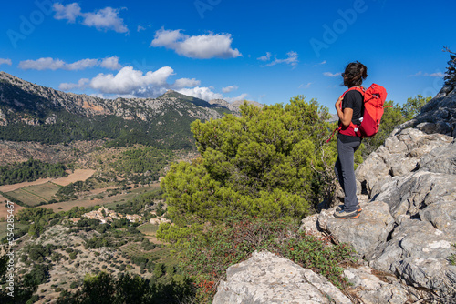 hiker woman with red backpack looking at the mountains and the valley, Orient valley , Bunyola, Majorca, Balearic Islands, Spain