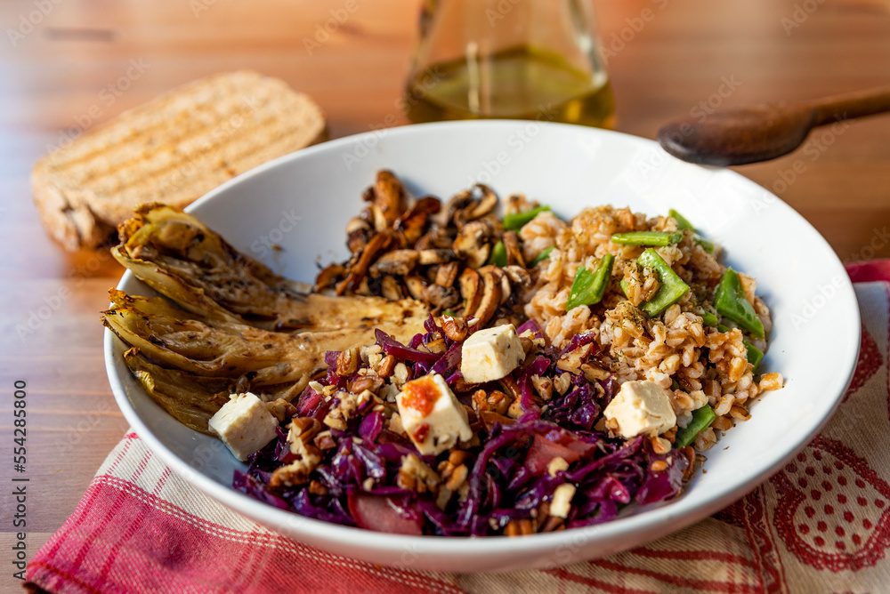 view of winter vegetarian bowl with red cabbage, mushrooms, tofu, spelt cereal, endive and radicchio on wooden table. Example of winter or autumn season homemade vegan dish