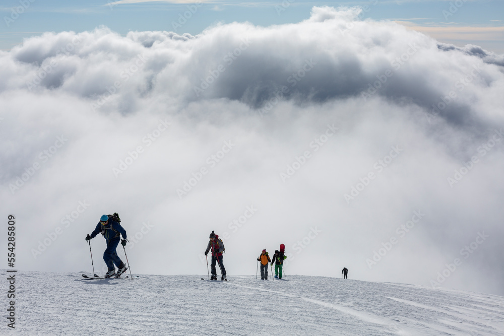 hikers with backpacks are on a high snow-covered peak above the clouds in the mountains. success achievement on the edge
