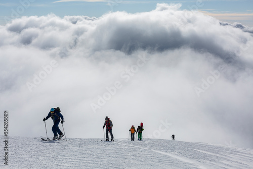 hikers with backpacks are on a high snow-covered peak above the clouds in the mountains. success achievement on the edge © almostfuture