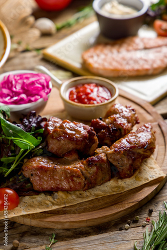 Kebab of pork with red onion and tomato sauce on wooden table macro close up vertical