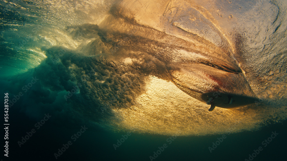 Surfer rides the wave and grabs the water surface. Underwater through the wave view of the surfer riding the wave and touching the water