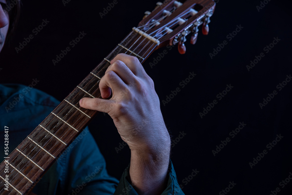 The guy in the dark shirt is plucking the strings of a six-string guitar The guy in the dark shirt is plucking the strings of a six-string guitar