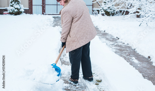 Winter problems concept . Woman digging snow with shovel at yard. Lady standing with blue shovel and cleaning snow .Winter routine concept