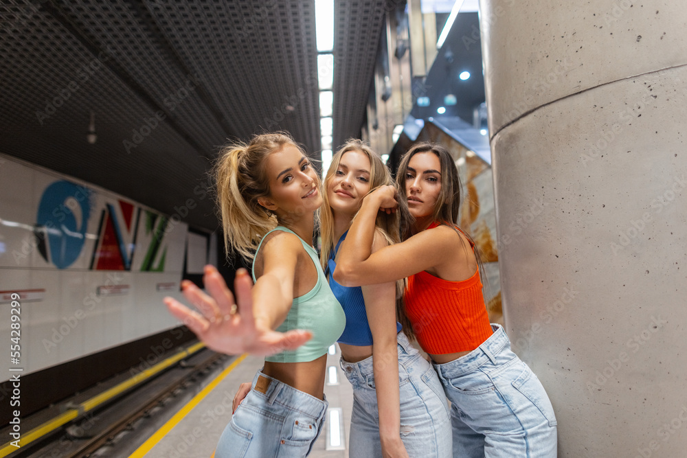 Beautiful young cheerful fashion girls in fashionable street clothes with tops and jeans standing and posing in the subway