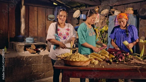 Mujer Xinca viendo a cámara mientras sus hermanas manipulan mazorcas de maíz. photo