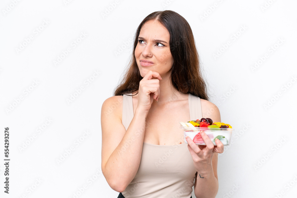 Young caucasian woman holding a bowl of fruit isolated on white background having doubts Young caucasian woman holding a bowl of fruit isolated on white background having doubts
