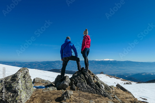 Couple with panoramic view of mountain hut Wolfsbergerhuette (Wolfsberger Huette) on Saualpe, Lavanttal Alps, Carinthia, Austria, Europe. Looking at snow covered Koralpe. Alpine road to remote cottage photo
