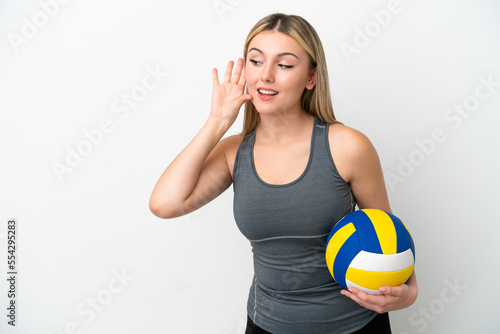 Young caucasian woman playing volleyball isolated on white background listening to something by putting hand on the ear
