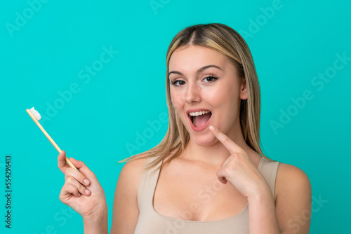 Young caucasian woman isolated on blue background with a toothbrush and happy expression