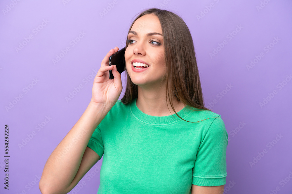 Young caucasian woman isolated on purple background keeping a conversation with the mobile phone Young caucasian woman isolated on purple background keeping a conversation with the mobile phone