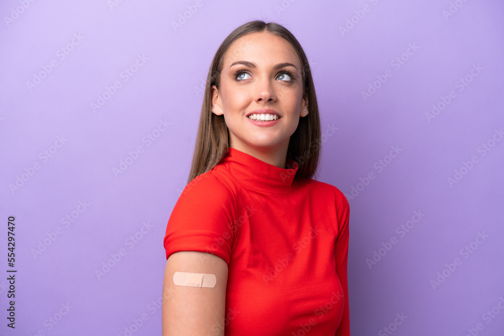 Young caucasian woman wearing band aid isolated on purple background looking up while smiling Young caucasian woman wearing band aid isolated on purple background looking up while smiling