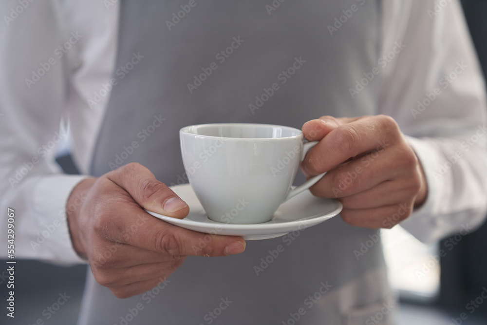 Your coffee, please. Cropped image of a man holding a cup of good coffee against the background of a gray apron. With a space to copy. High quality photo Your coffee, please. Cropped image of a man holding a cup of good coffee against the background of a gray apron. With a space to copy. High quality photo