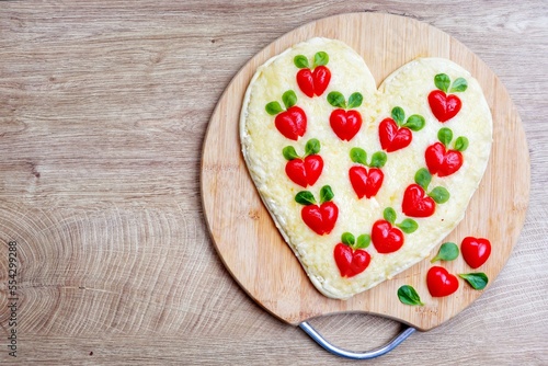 Heart shaped pizza with heart shaped tomatoes on wooden cutting board with wooden background.Creative art food idea for celebrate Valentine or Mother day.Top view.Copy space