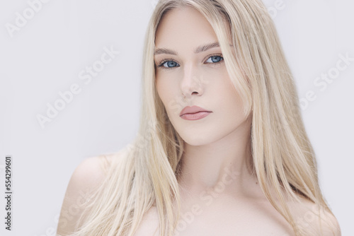 Young woman with straight blonde hair, blue eyes, clear skin with natural make up, poses against a white backdrop.