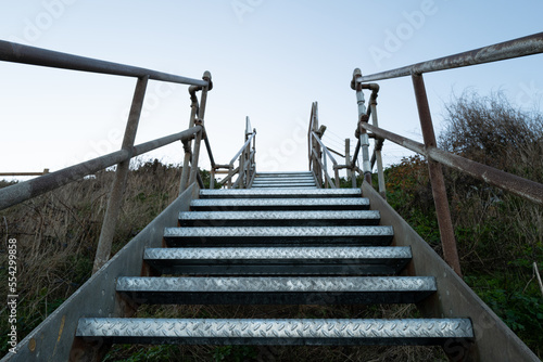 Fototapeta Naklejka Na Ścianę i Meble -  Vertical view of a cliff edge metal staircase seen ascending to the top of the cliff. The staircase is dangerous in wet conditions.