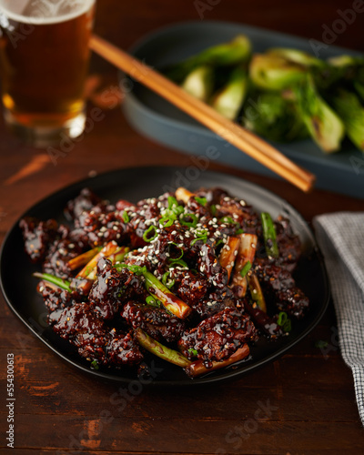 General Tso's chicken with scallions, sesame seeds on a black plate.
