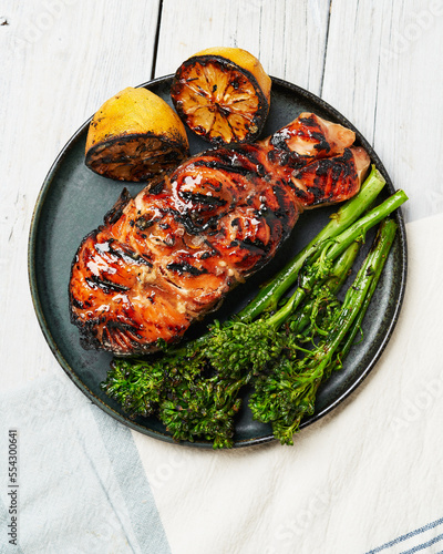 Grilled salmon fillet with char marks, served with broccolini and lemon on a modern plate, a healthy and flavorful meal option.