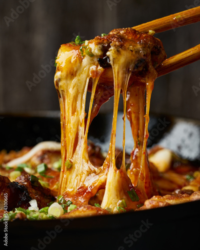 Cheesy buldak, a spicy Korean chicken dish, being lifted with chopsticks, showing off the stringy, melted cheese.