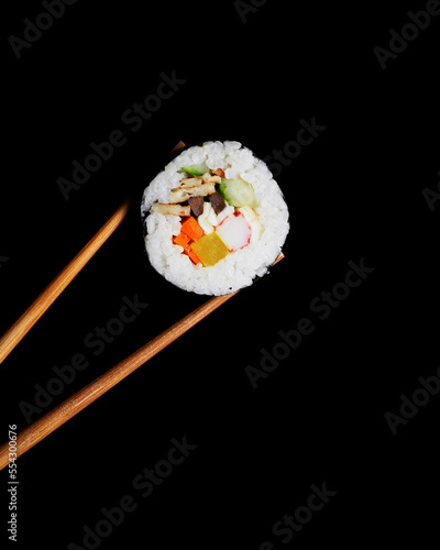 A piece of kimbap held by chopsticks against a black background, highlighting the colorful fillings of this Korean delicacy.