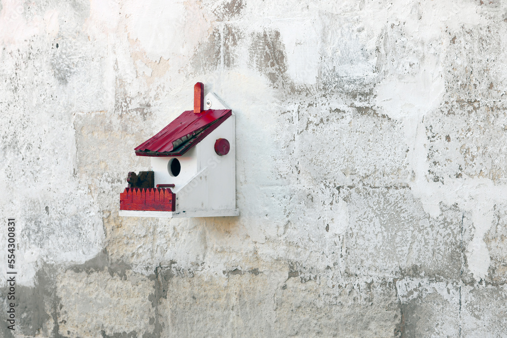 Hand crafted wooden bird house shelter for birds hanging on a white wall Hand crafted wooden bird house shelter for birds hanging on a white wall
