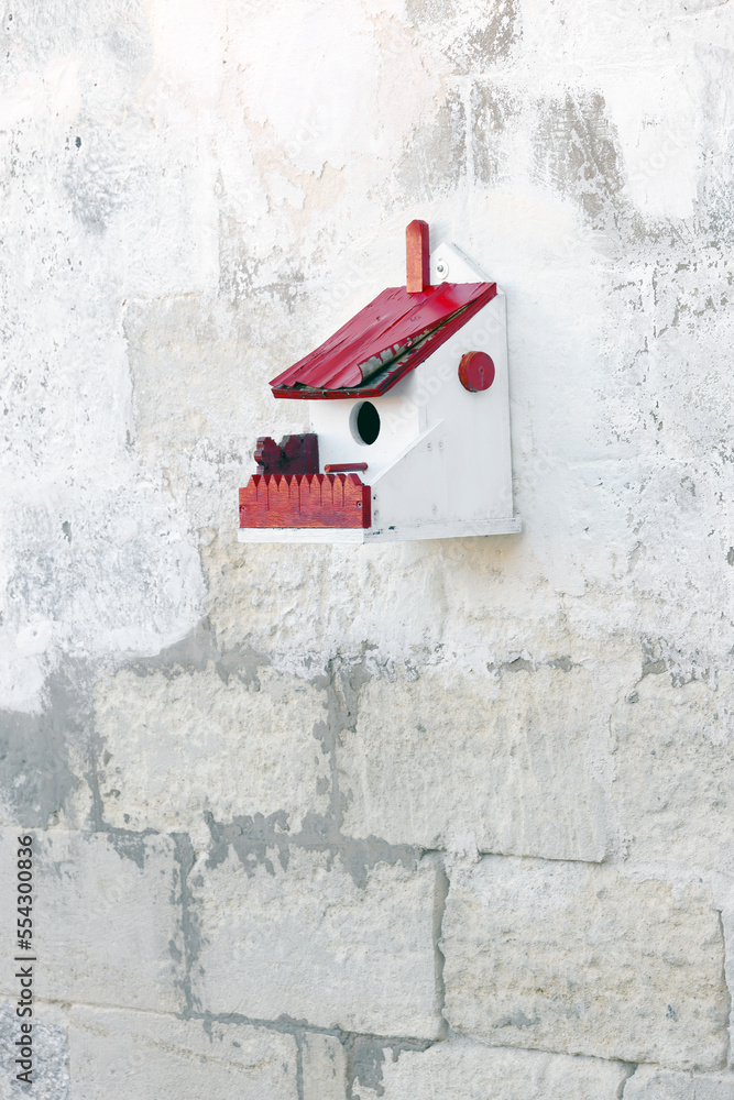 Hand crafted wooden bird house shelter for birds hanging on a white wall Hand crafted wooden bird house shelter for birds hanging on a white wall