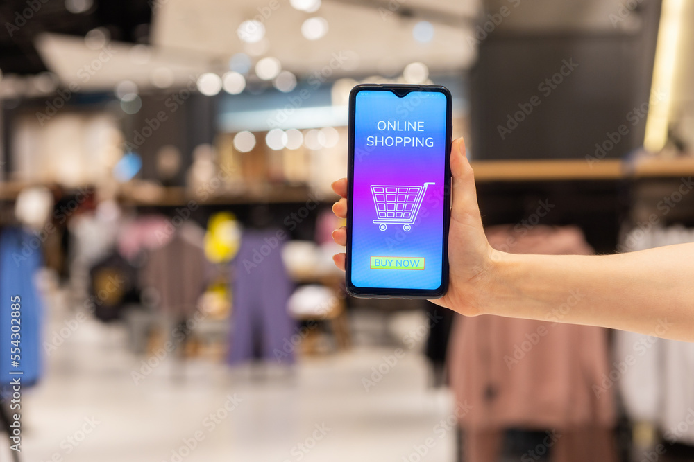 Obraz premium Marketing and advertising. Close-up of woman's hand showing smartphone with purchases in online store. Clothes store at background. Concept of shopping and discounts