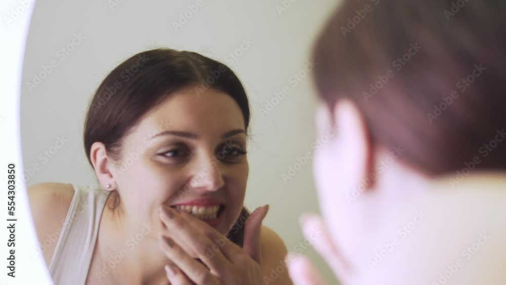 Young woman looking in big mirror at teeth, having dental problems, stomatology Young woman looking in big mirror at teeth, having dental problems, stomatology