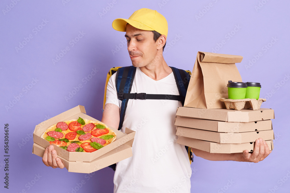 Portrait of hungry man courier holds pizza boxes in hand isolated on purple background, looking at tasty fast food with sticking tongue, wants to eat while delivering orders. Portrait of hungry man courier holds pizza boxes in hand isolated on purple background, looking at tasty fast food with sticking tongue, wants to eat while delivering orders.
