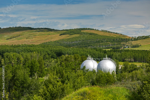 Two spherical white oil storage tanks amongst trees and hills with clouds and blue sky; Turner Valley, Alberta, Canada photo