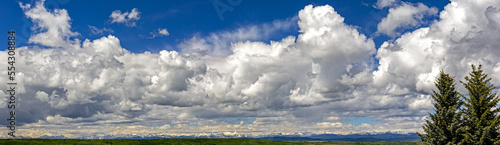 Panorama of large storm clouds with blue sky and the Rocky mountains in the distance; Calgary, Alberta, Canada photo