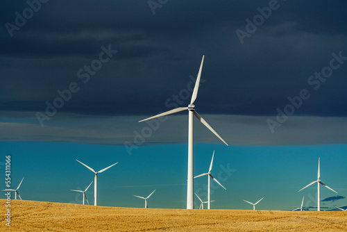Large metal wind turbines in a rolling stubble field with Chinook arc and blue sky, North of Glenwood, Alberta; Alberta, Canada photo